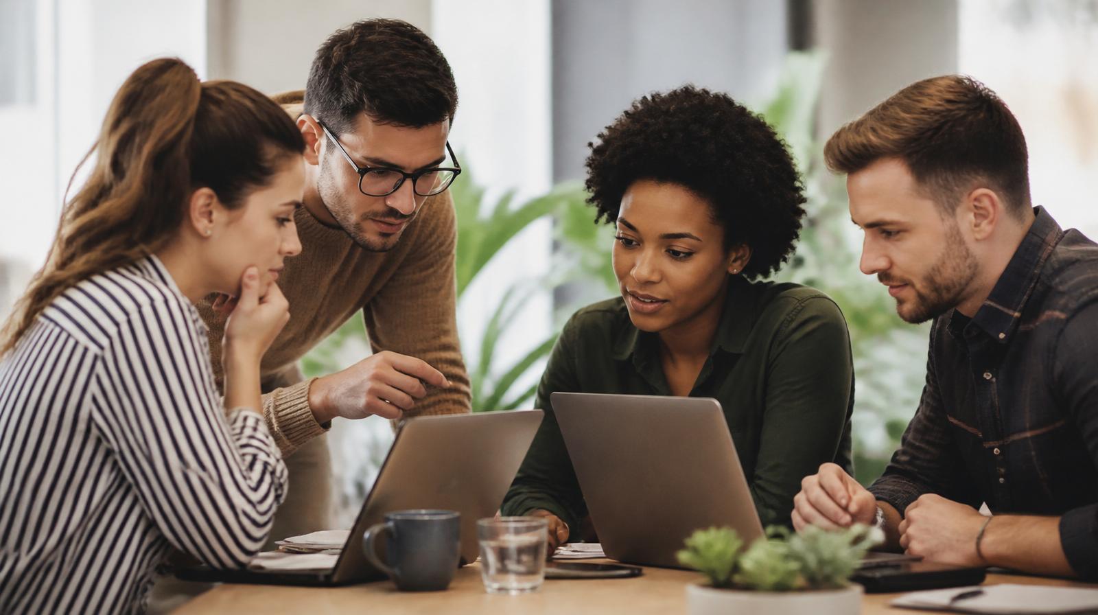 Equipo de trabajo colaborando con portátiles en una oficina luminosa